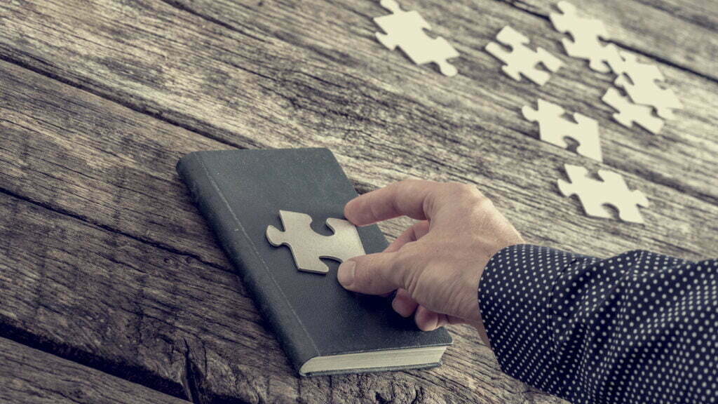 Person placing a puzzle piece on top of a book.